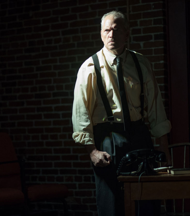 Man in suspenders standing, looking intense